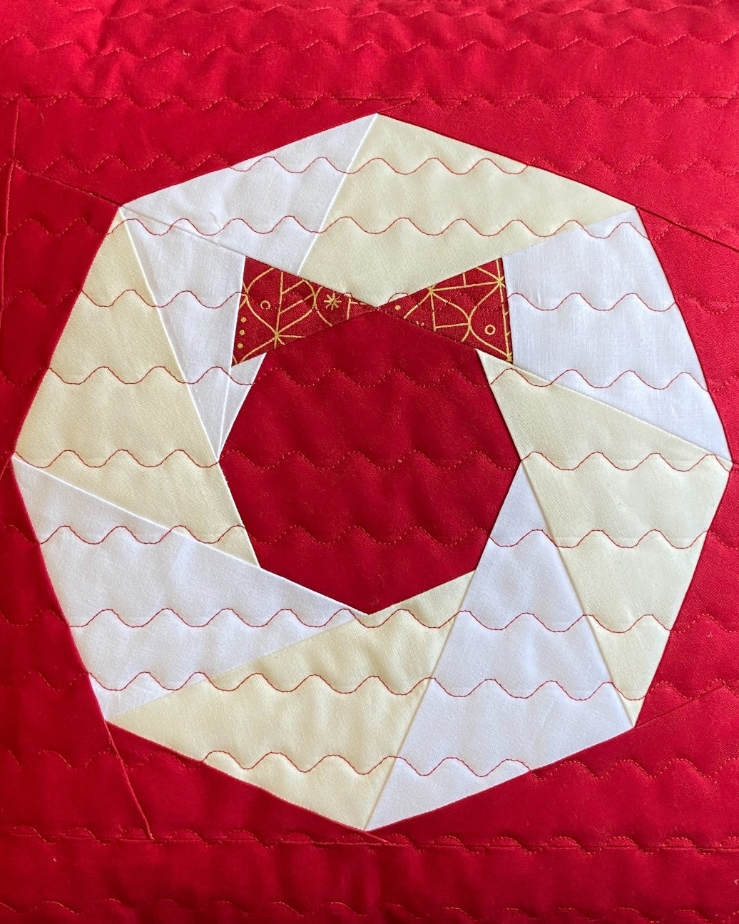 Close-up of the foundation paper pieced wreath on a red pillow with cream and white wavy quilting and red bow