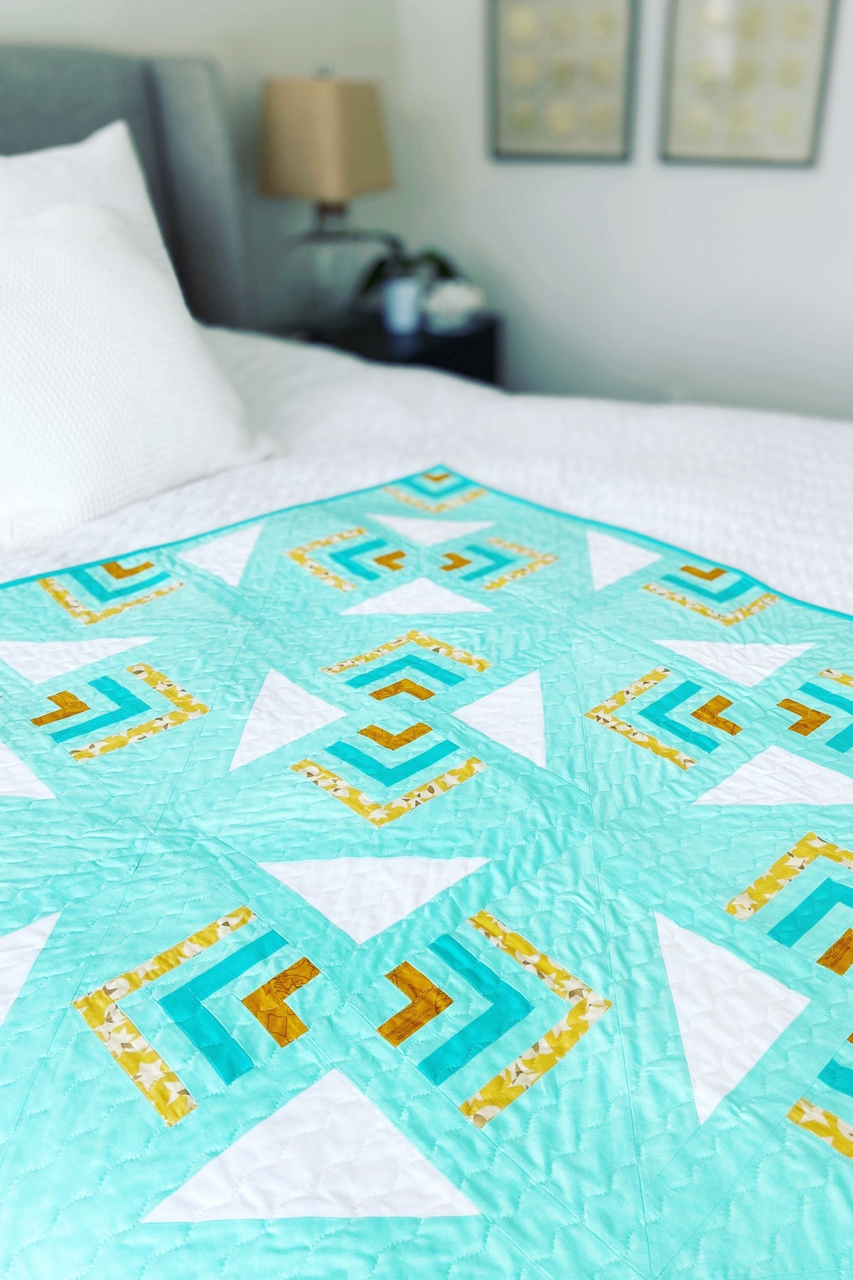 Aqua Lucky Twist quilt with gold, teal and white accents spread on a bed with white bedding