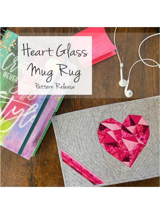 Heart Glass Mug Rug pattern release graphic: pink faceted heart on gray mug rug on a wood desk with books and earbuds