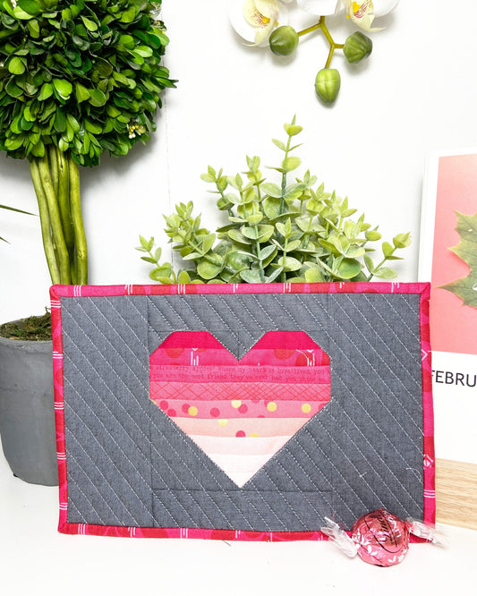 Startled Heart mug rug in pink striped heart on gray with pink binding, with plants and a candy